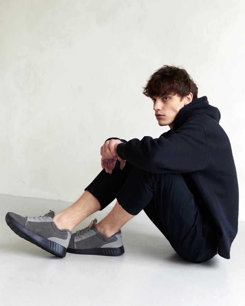 Junger Mann am Boden sitzend mit Merino Sneaker in grau mit schwarzer Sohle an den Füßen