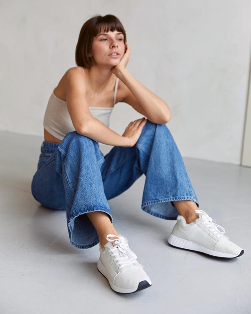 Junge Frau auf dem Boden sitzend mit Merino Sneaker in weiß an den Füßen
